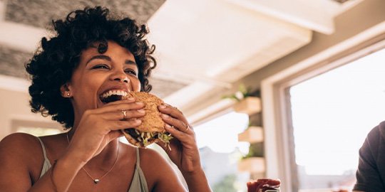 Woman joyfully enjoying a sandwich after removing her Invisalign