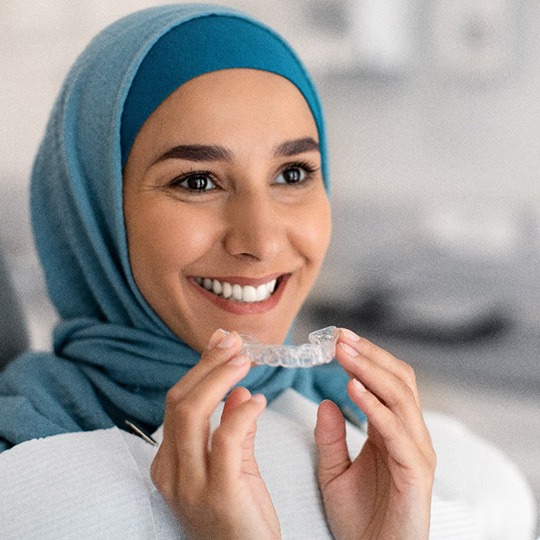 Woman in blue hijab smiling inserting Invisalign